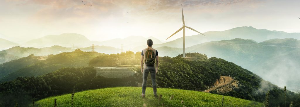 Mies katsoo kukkulalta maisemaa, jossa näky kukkuloita ja moderni tuulimylly.