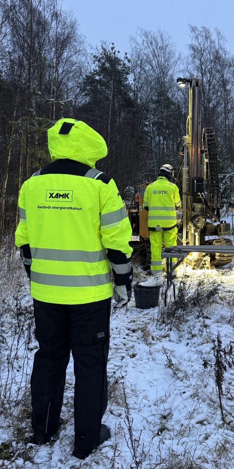 Metsämaastossa suuri pora ja työvaatteisiin pukeutuneita ihmisiä.