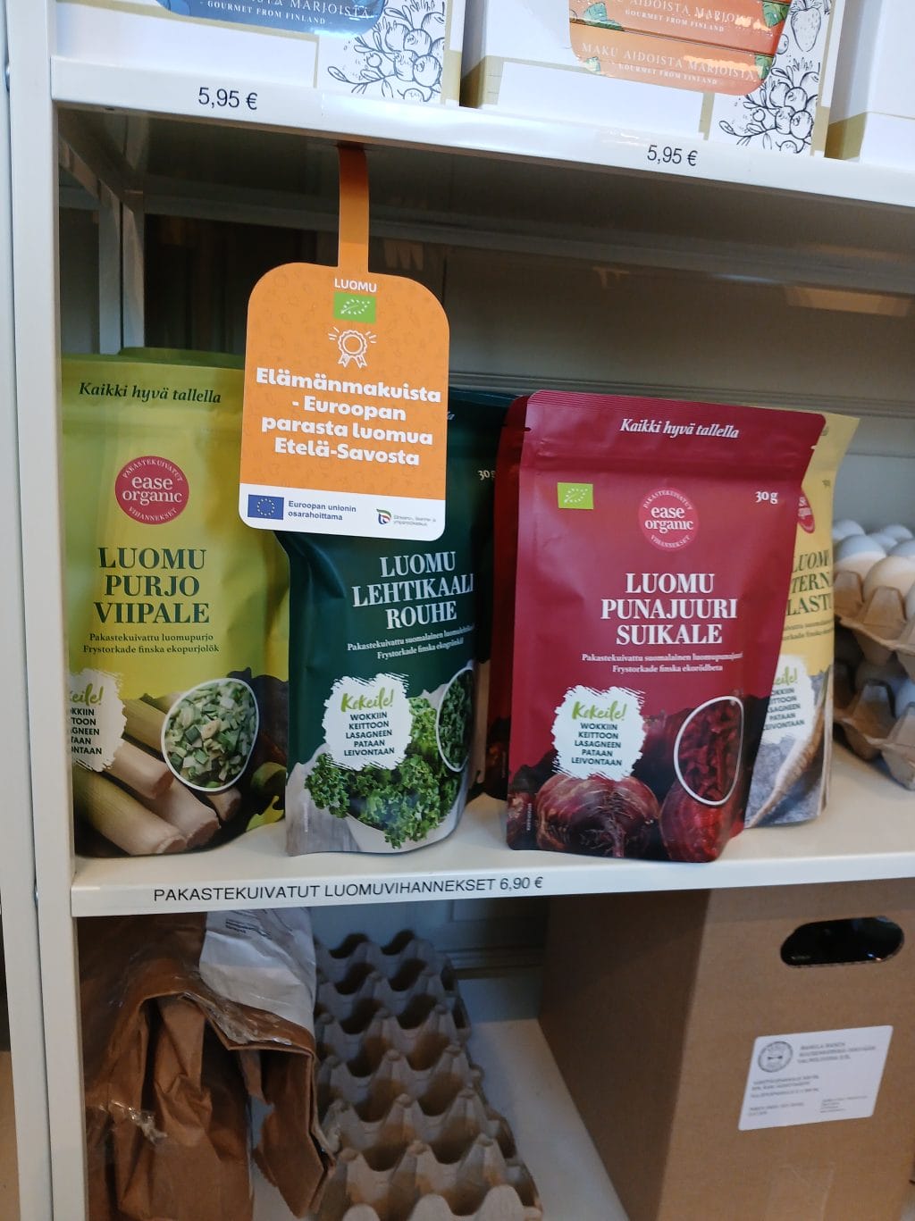 Hyllyllä kolme eri väristä pussia. Niiden edessä on kelta-oranssi ns. hyllyvippa, joka on kiinnitetty ylemmän hyllyn alalaitaan.