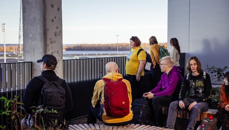 Valokuva. Nuoria henkilöitä istumassa ja katselemassa ikkunasta merelle.