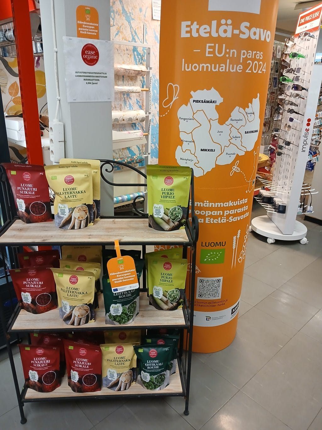 Kuvassa iso pahvimainos ja sen vieressä hylly, jolla on pusseja.