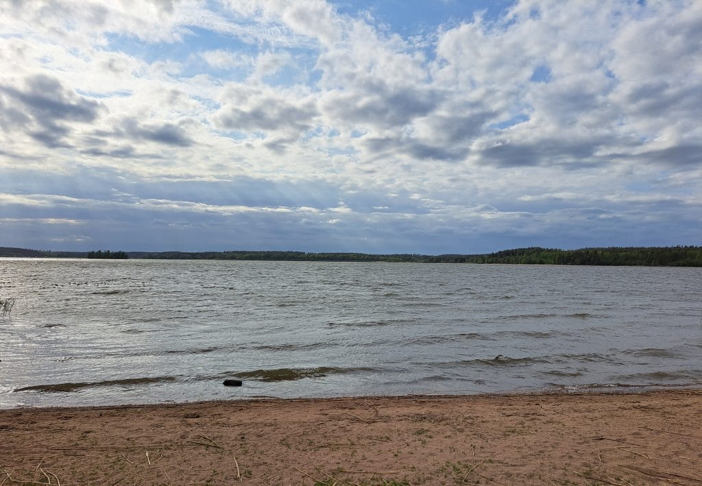 Hiekkaranta järvimaisema ja pilvinen taivas