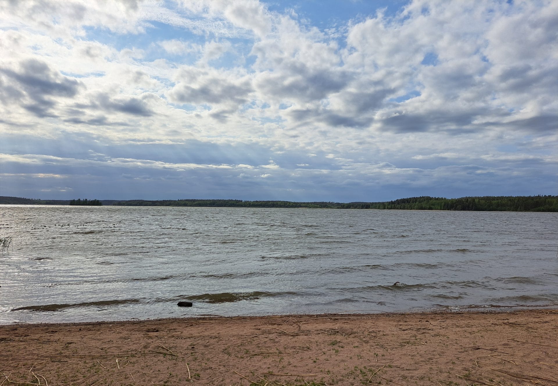 Hiekkaranta järvimaisema ja pilvinen taivas