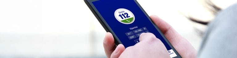 Puhelin, jossa on avattuna 112-sovellus, ja käsi näppäilemässä sitä.