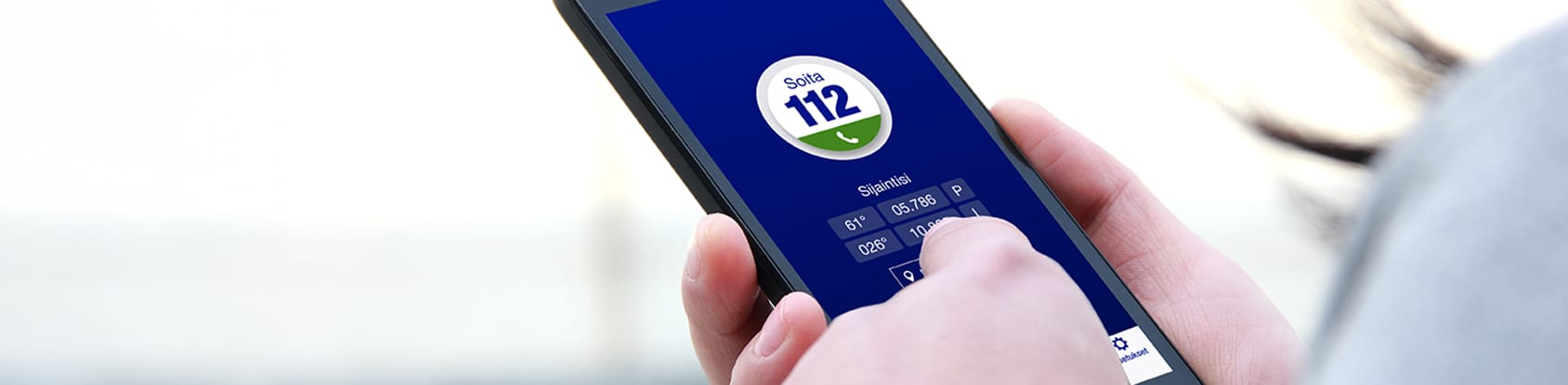 Puhelin, jossa on avattuna 112-sovellus, ja käsi näppäilemässä sitä.