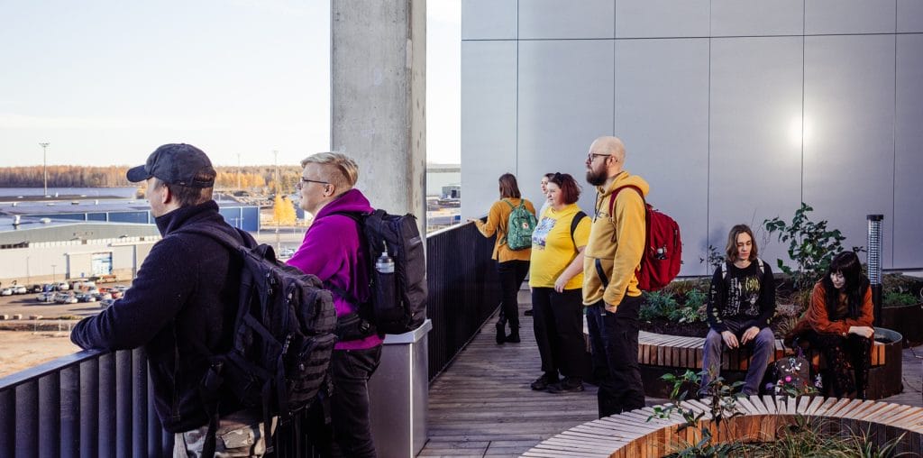 Valokuva. Nuoria aikuisia rakennuksen parvekealueella, katseet merelle.