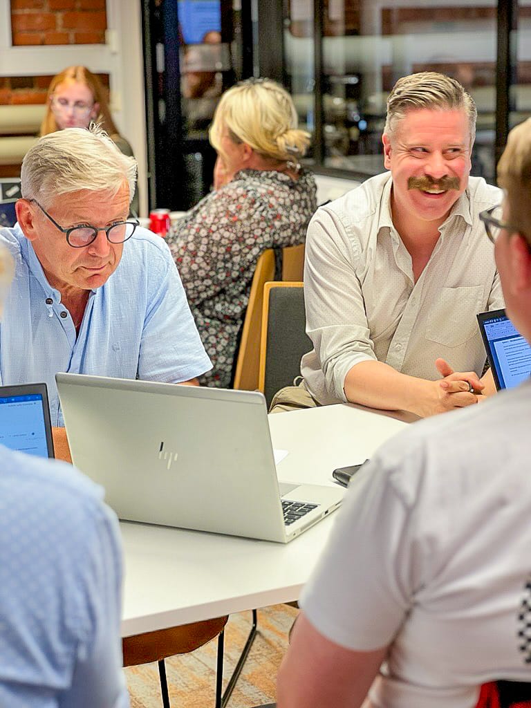 Yrittäjiä työpajassa istumassa läppäreineen pöydän ääressä.