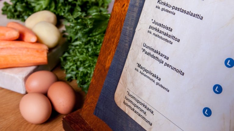 Pöydällä näkyy etualalla ruokalistan alalaita ja taustalla ruokien raaka-aineita. Kuva: Darcmedia