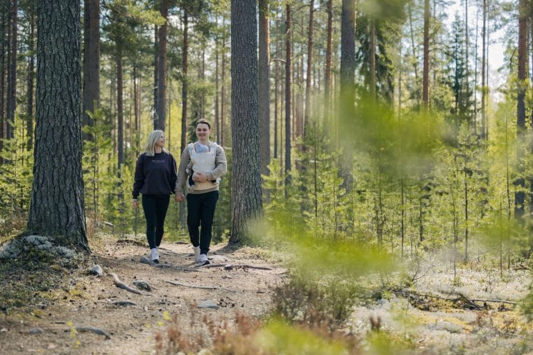Vanhemmat ja vauva kävelevät metsässä, vauva on kantorepussa