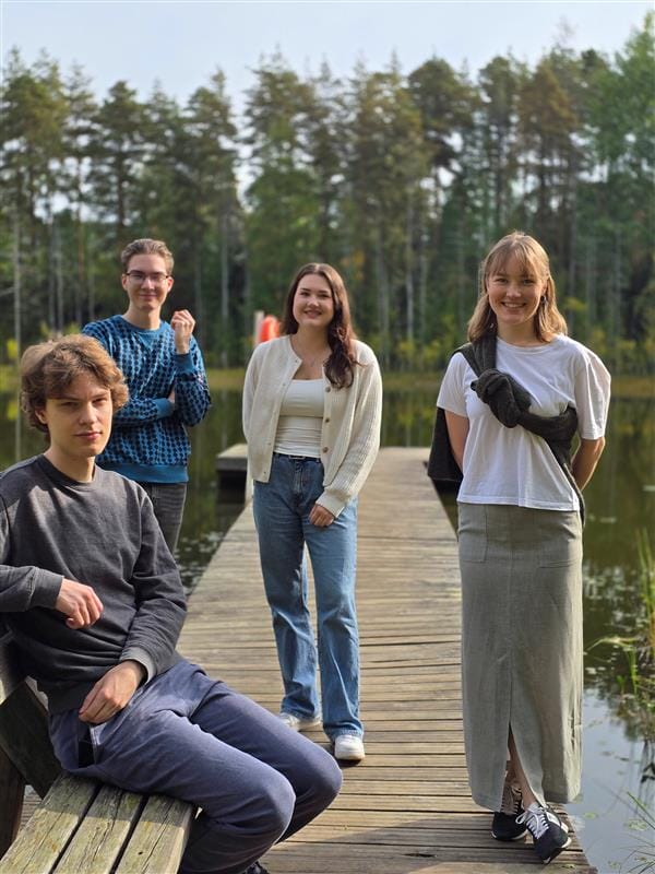 Ryhmäkuva laiturilla. Taustalla järvi ja vihertäviä puita,
