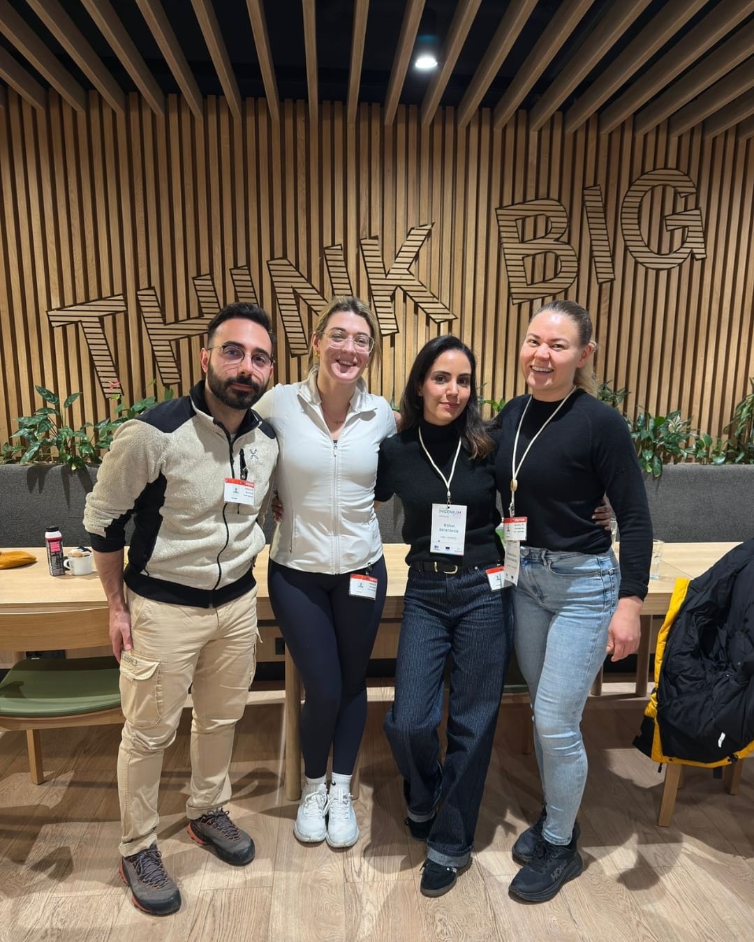 Kolme osallistujaa Katariinan kanssa seisovat ja hymyilevät iloisesti. Heidän takana seinällä lukee Think Big.