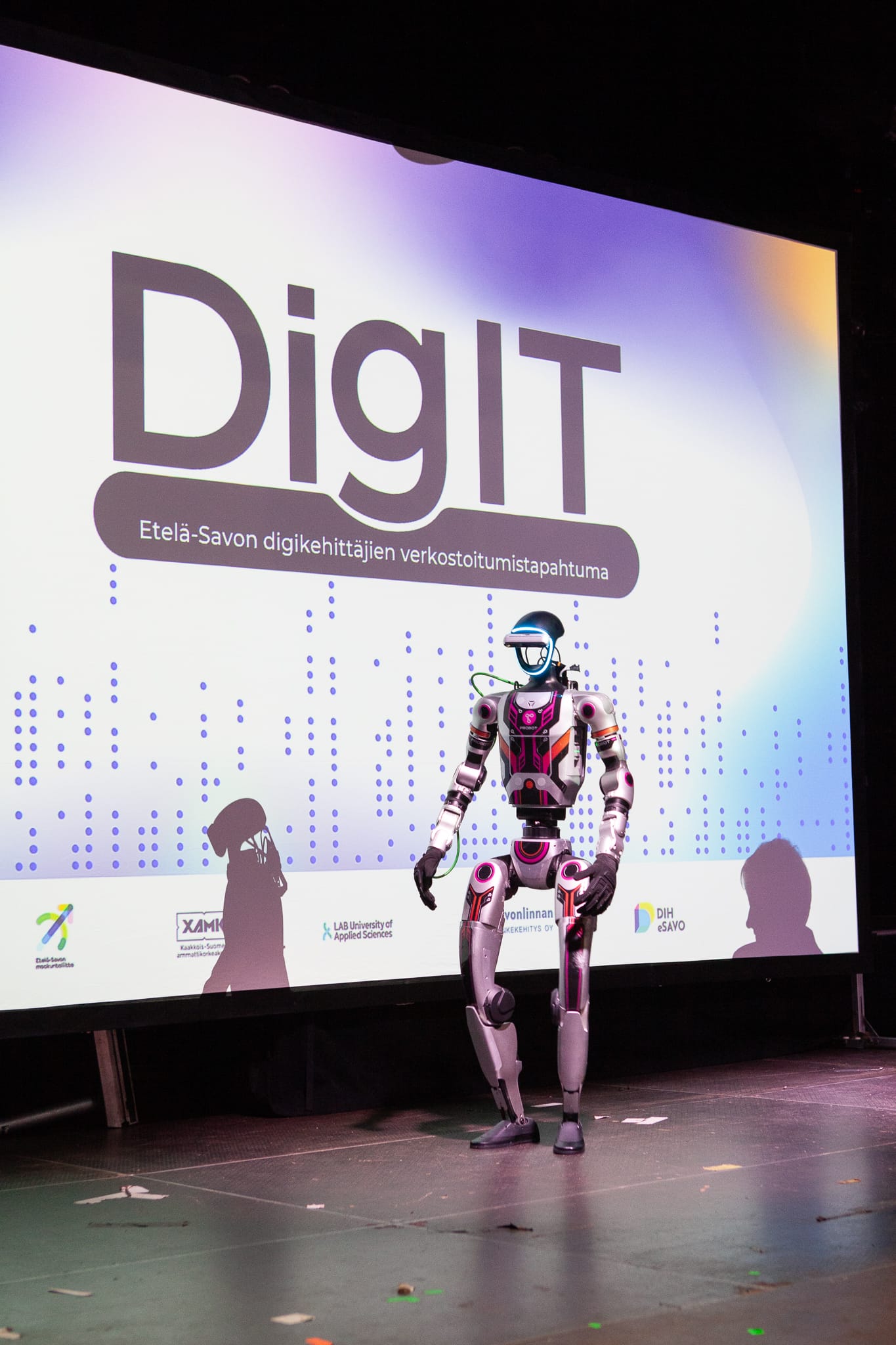 Humanoidirobotti Unitree G1 DigIT-tapahtuman lavalla. Lavan valkokankaalle heijastettuna DIGIT-tapahtuman logo.