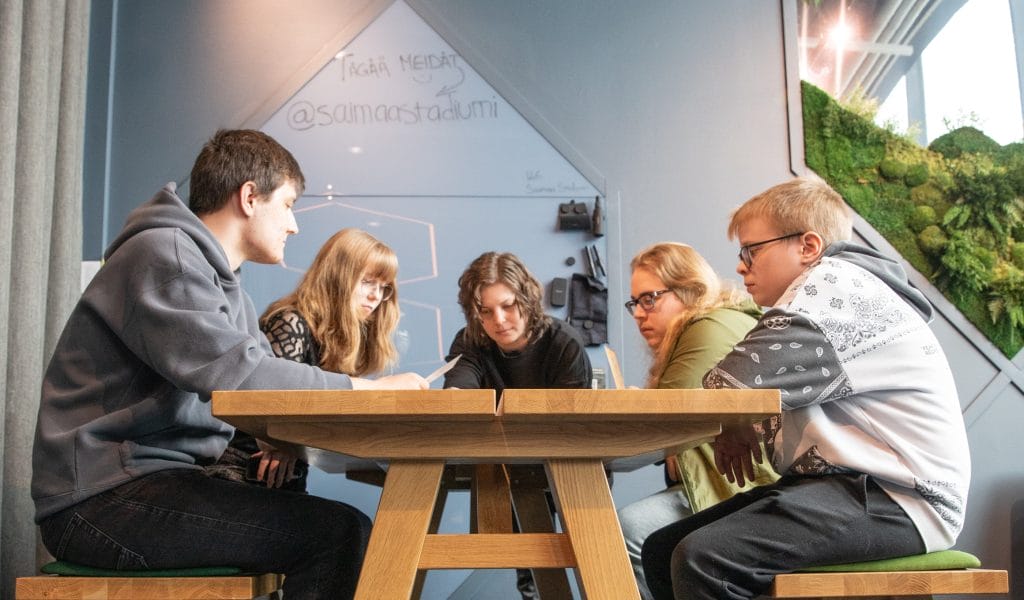 Valokuva. Nuoria pöydän ympärillä. Yhdessä kirjoittamisen tunnelma.