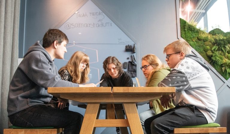 Valokuva. Nuoria pöydän ympärillä. Yhdessä kirjoittamisen tunnelma.