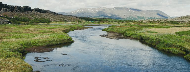 Kuvan keskellä joki, jonka pakopisteen takana näkyy vuori. Ympärillä vihreää ruohoa.