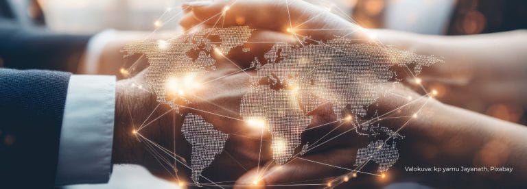 Kaksi ihmistä puristaa kätensä yhteen, etualalla osa maailmankarttaa.