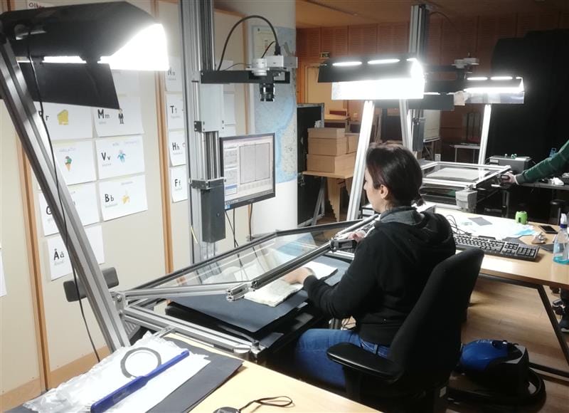 Henkilö istuu tasoskanneridigitointilaitteen ääressä toimistoympäristössä.