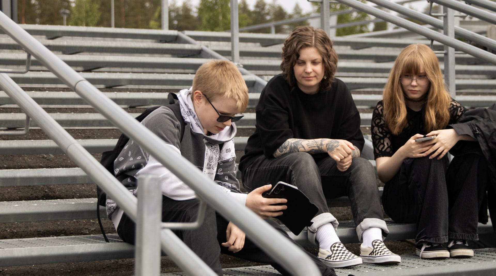 Valokuva. Nuoria henkilöitä portailla. Katseet kännykässä. Rauhallinen tunnelma.