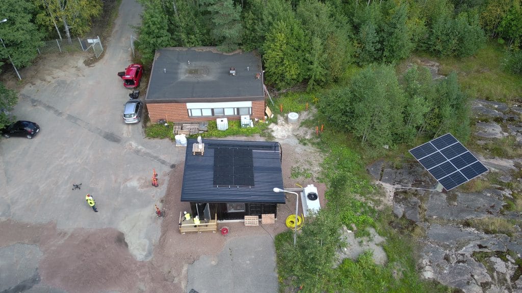 Ilmakuva kahdesta rakennuksesta metsäisessä ympäristössä.