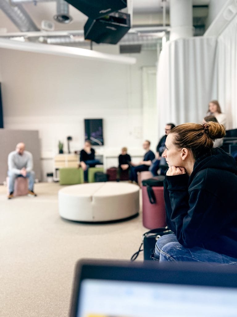 Ihmisiä istumassa Kouvolan Fuel-tilan katsomossa. Henkilö etualalla nojaa käsiin ja katsoo esitystä.