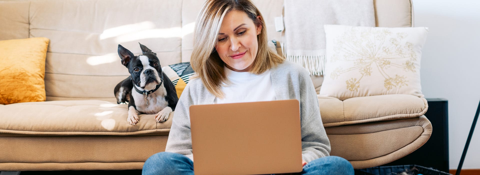 Nainen istuu lattialla sohvan edessä läppärin kanssa.