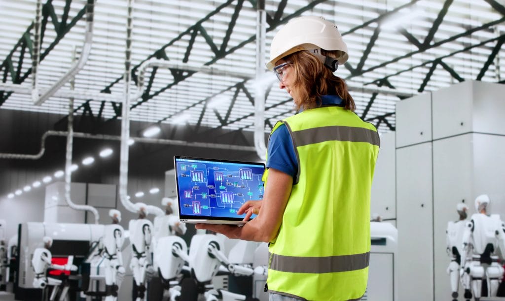 Etualalla huomioliivi päällä oleva insinööri, joka ohjaa tietokoneellaan taustalla olevia humanoideja.