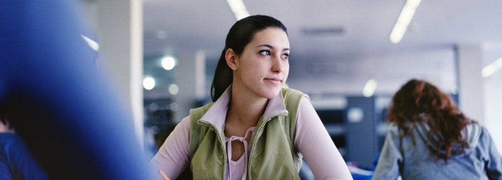 Nuori nainen istuu luokassa ja katsoo pohdiskellen oikealle.