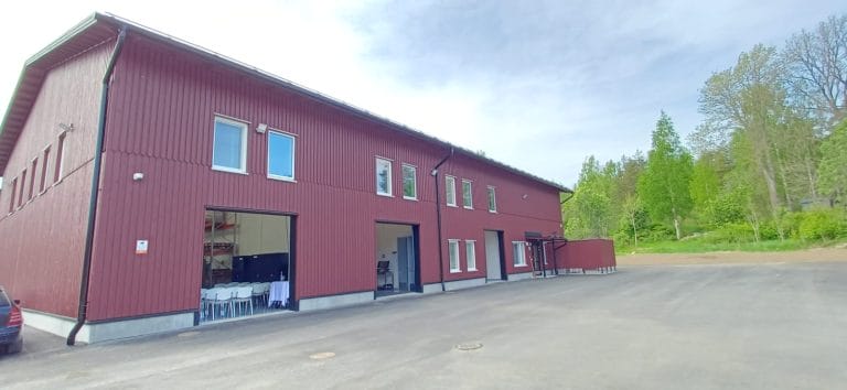 Punainen hallirakennus kesäisessä maisemassa.