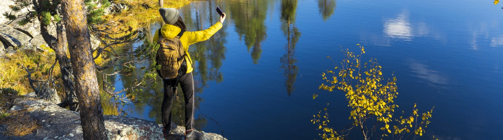 Nainen ottaa selfien järven rannalla syksyllä.