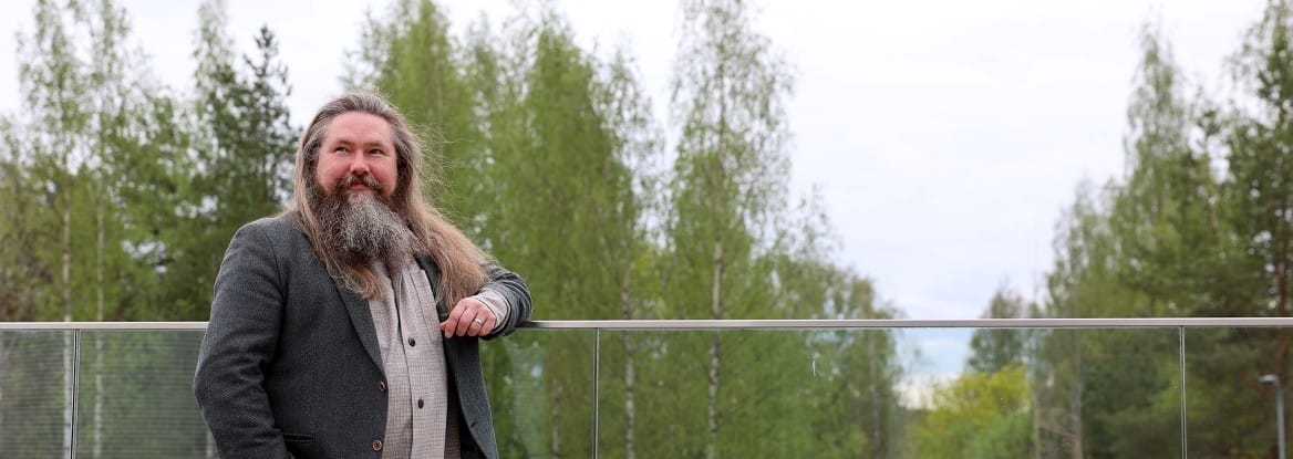 Henkilö ulkona, kesäisiä puita takana.