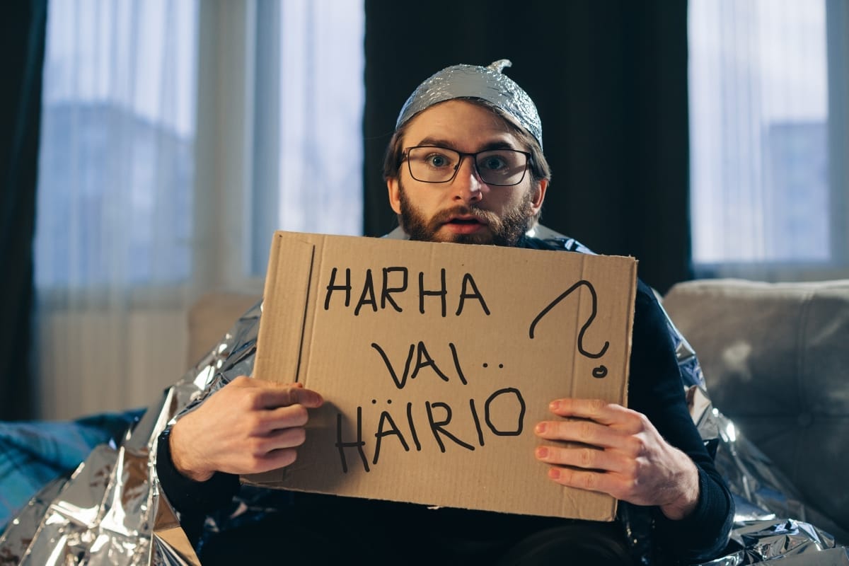 Harha vai häiriö webinaarit syksyllä 2026 kuvituskuva. Foliohattuinen mies pitää pahvikylttiä, jossa lukee harha vai häiriö. Kuva: Adobe Stock.