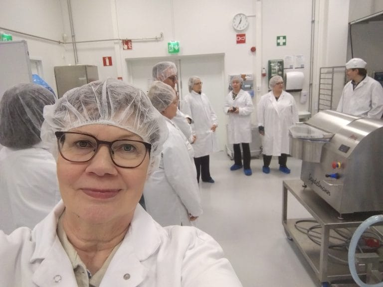 Valkoisiin takkeihin ja myssyihin pukeutunut joukko ihmisiä valkoisessa huoneessa. Etualalla nainen.