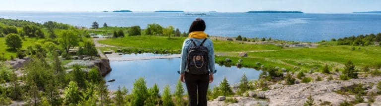 Nainen seisoo selin kalliolla katsellen merimaisemaa.