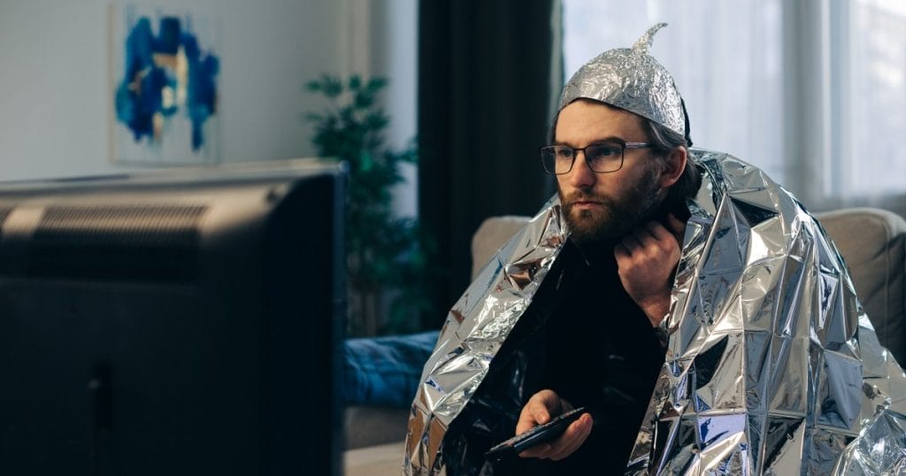 Harha vai häiriö webinaarisarjan kuvituskuva AdobeStock. Mies katselee televisiota foliohattu ja -viitta päällä.