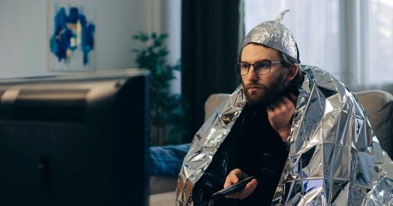Harha vai häiriö webinaarisarjan kuvituskuva AdobeStock. Mies katselee televisiota foliohattu ja -viitta päällä.