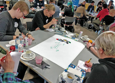 Opiskelijoita ja yritysten edustajia työpajassa Digiverstaalla. Yhteisen pöydän ääressä piirretään kuvia ja kirjoitetaan suunnitelmia.
