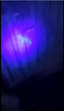 Kuva kaikugrammi-pelistä, jossa seinään uv-tussilla kirjoitettu koodi on paljastettu uv-taskulampun valokeilassa.
