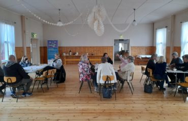 Kuvassa ihmisiä istumassa kolmessa pöydässä ja keskustelemassa Tiutisen työväentalolla huhtikuussa 2022.