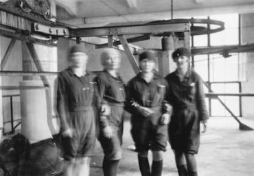 Mustavalkoisessa kuvassa neljä naista työvaatteissa tehtaalla. Yhtyneet Paperitehtaat, Myllykoski, puuhiomo 1930. Lusto, Suomen Metsäyhdistyksen kokoelma, Metsätaloudellinen Valistustoimisto.