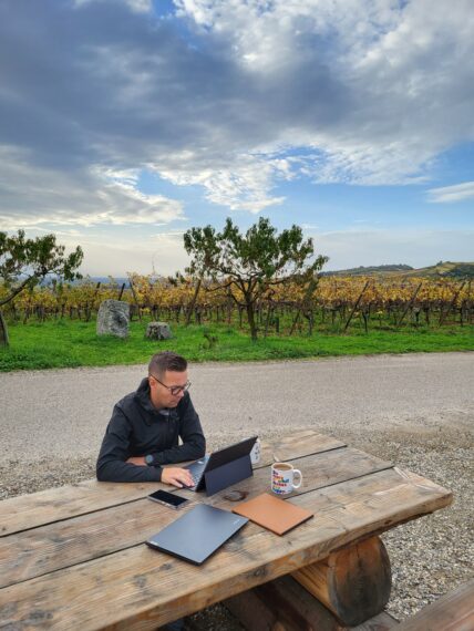 Henkilö viinitarhan edessä opiskelemassa kannettavalla tietokoneella
