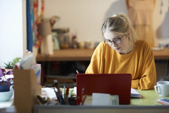 keltapaitainen ja silmälasipäinen nainen on kannettavan tietokoneen ääressä