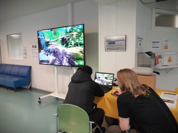 Sairaalan käytävälle rakennettu virtuaaliluontopiste, joka sisältää tietokoneen ja suuren näytön. Kaksi ihmistä ohjaa tietokoneelta luontokokemusta, joka näkyy muille heidän vasemmalla puolellaan olevasta näytöstä.